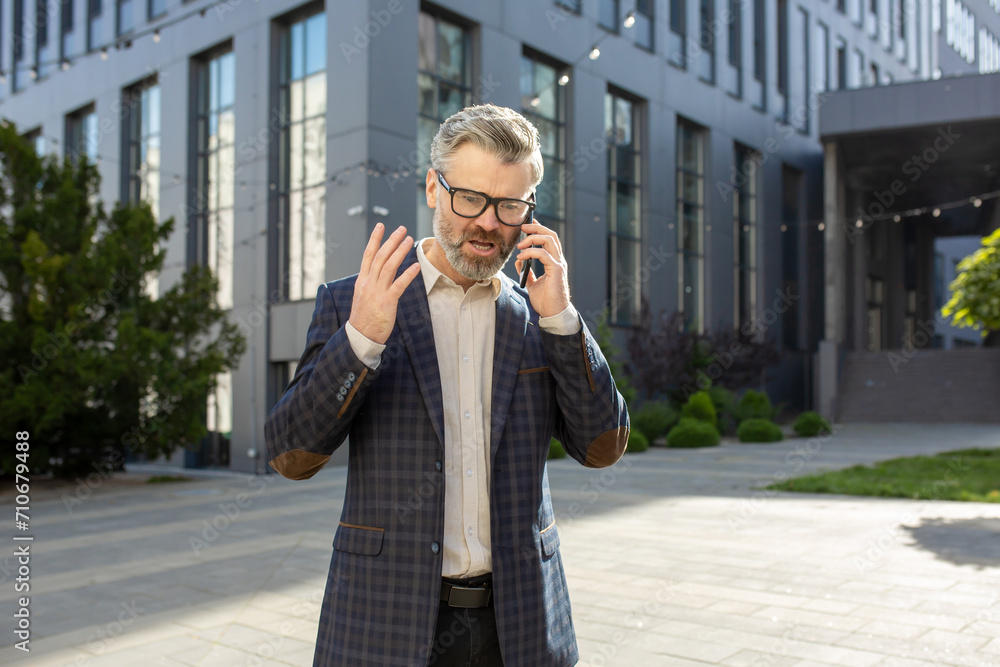 A senior executive in a checkered suit talks on his mobile phone, discussing important business while standing near an office building. A senior executive in a checkered suit talks on his mobile phone, discussing important business while standing near an office building.