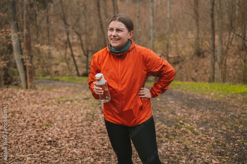 Young female hiker drinking water from reusable bottle after a quick jogging workout in autumn forest