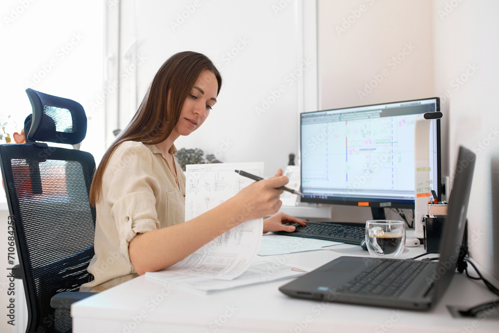 Portrait of a remote worker. An adult woman sits at a table in front of a computer and draws up a costly estimate. Confident young lady freelancer working from home.