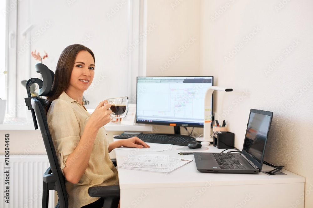 Portrait of a remote worker. A beautiful smiling brunette girl sits at a table in front of a computer and works with a layout. Confident young lady freelancer working from home. Portrait of a remote worker. A beautiful smiling brunette girl sits at a table in front of a computer and works with a layout. Confident young lady freelancer working from home.