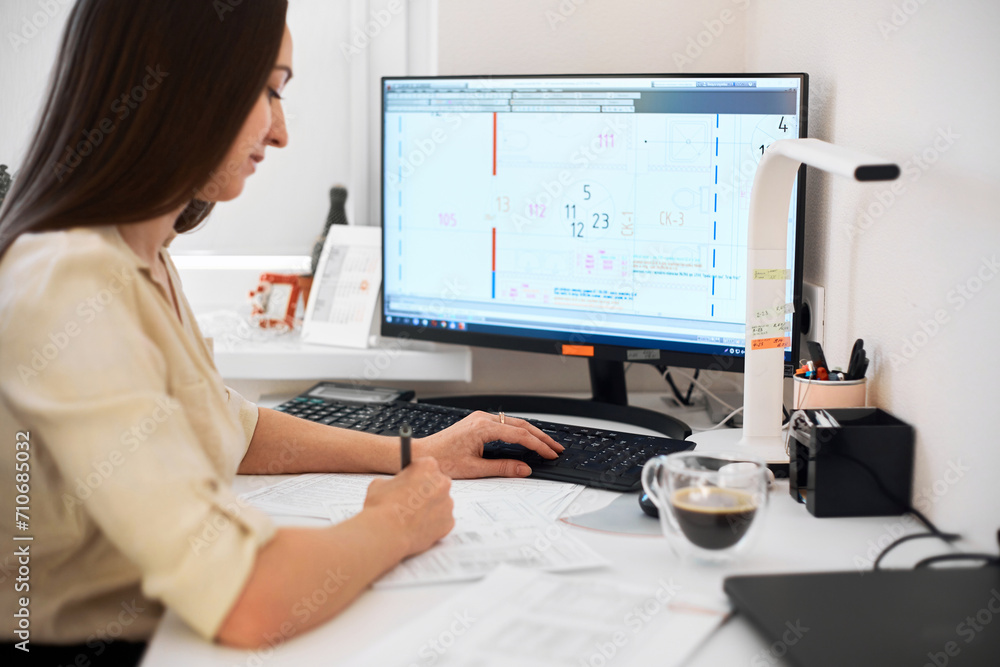 Portrait of a remote worker. An adult woman sits at a table in front of a computer and draws up a costly estimate. Confident young lady freelancer working from home. Portrait of a remote worker. An adult woman sits at a table in front of a computer and draws up a costly estimate. Confident young lady freelancer working from home.