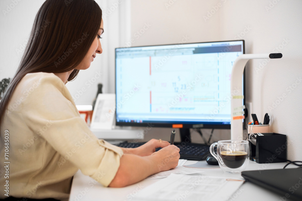 Portrait of a happy female designer estimator sitting at the table with a notebook and calculator, counting the balance and typing on a laptop, finishing her work with a cup of coffee. Portrait of a happy female designer estimator sitting at the table with a notebook and calculator, counting the balance and typing on a laptop, finishing her work with a cup of coffee.