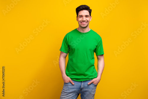 Photo of cheerful happy smiling guy in green t shirt put hands denim jeans posing candid person isolated over yellow color background