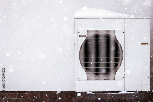 Heat Pump Covered Snow in Winter. Efficient Electric Heater Outside House in Snowy Winter. Modern Heating System Home. Low-Energy House. Copy Space.