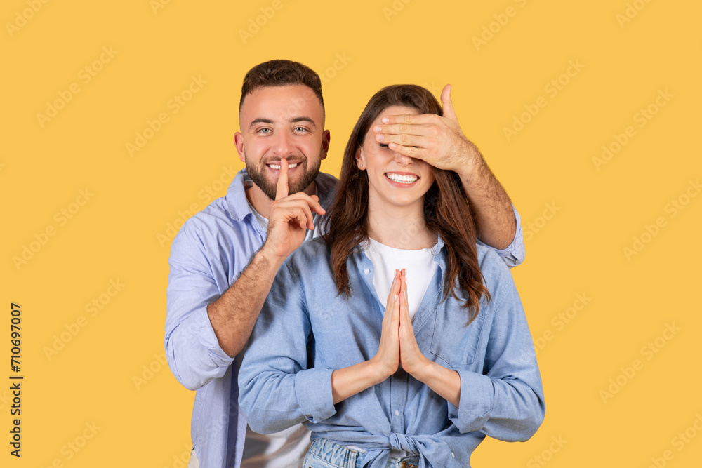 Man with finger on lips covering woman's eyes in playful surprise gesture Man with finger on lips covering woman's eyes in playful surprise gesture
