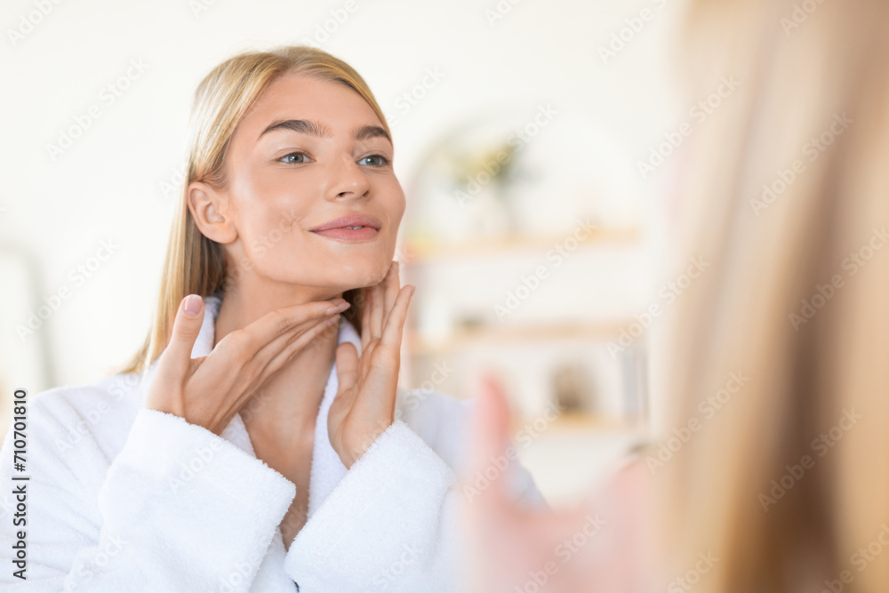 blonde lady in modern bathroom applying cream to her neck blonde lady in modern bathroom applying cream to her neck
