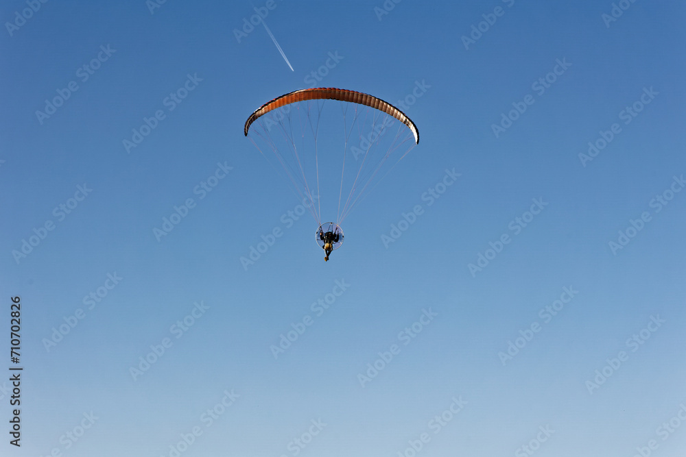 Motorized paraglider flying against the blue sky with clouds, outdoor activity, extreme sports, extreme sports, paraglider flying in the sun in the sky. The sport of paragliding Motorized paraglider flying against the blue sky with clouds, outdoor activity, extreme sports, extreme sports, paraglider flying in the sun in the sky. The sport of paragliding