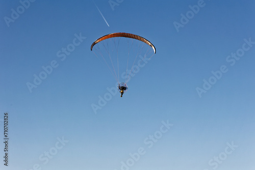 Motorized paraglider flying against the blue sky with clouds, outdoor activity, extreme sports, extreme sports, paraglider flying in the sun in the sky. The sport of paragliding