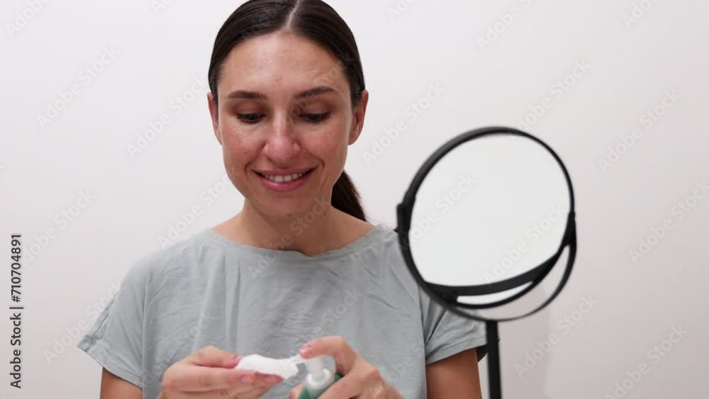 millennial young woman is doing at home facial procedure, remove makeup with hydrophilic oil and cotton disk,massaging face with roller and cleaning with ultrasound device.girl using mirror. millennial young woman is doing at home facial procedure, remove makeup with hydrophilic oil and cotton disk,massaging face with roller and cleaning with ultrasound device.girl using mirror.