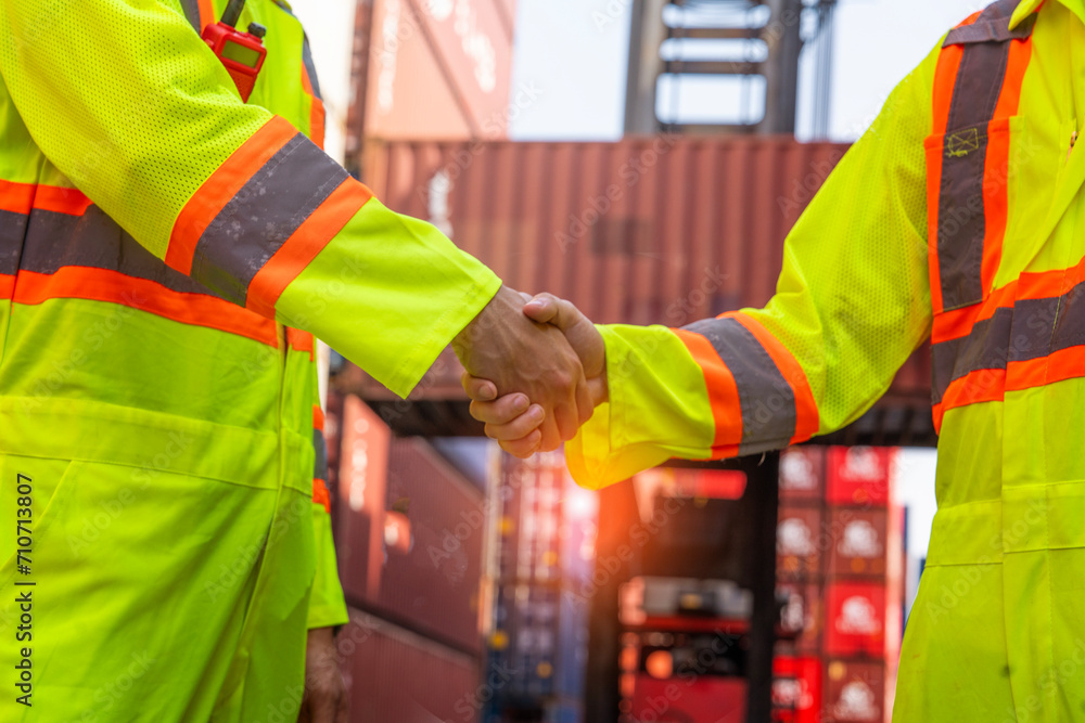 male worker wearing a reflective uniform loads a container, shaking hands with a colleague engineer working together successfully in the container yard.