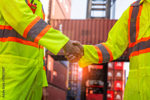 Obraz na płótnie male worker wearing a reflective uniform loads a container, shaking hands with a colleague engineer working together successfully in the container yard. w salonie