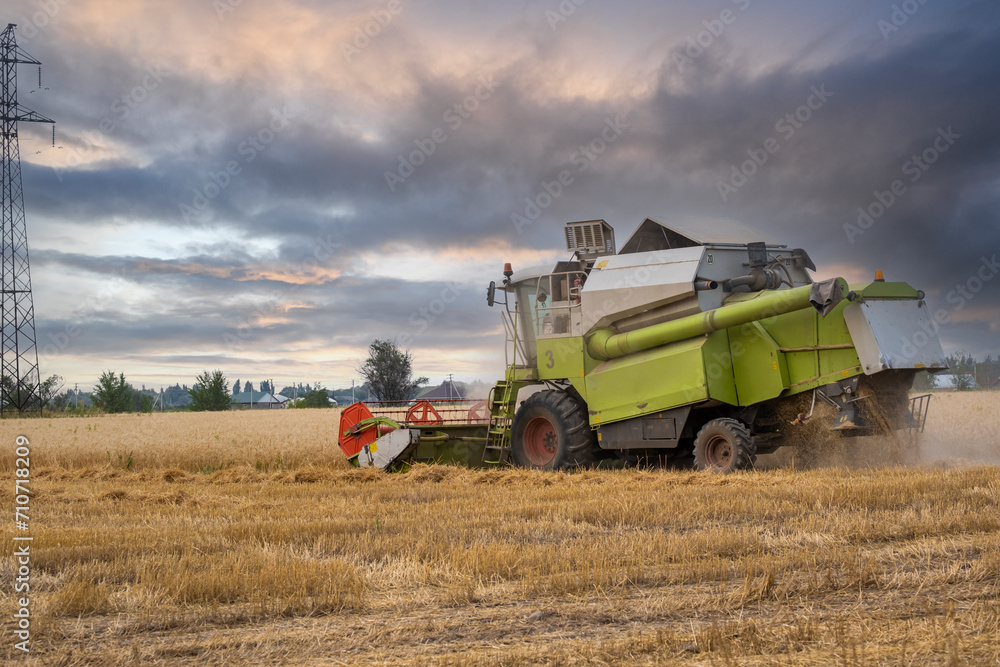 A combine harvester harvests in a wheat field against the backdrop of an epic sunset before the rain. A combine harvester harvests in a wheat field against the backdrop of an epic sunset before the rain.