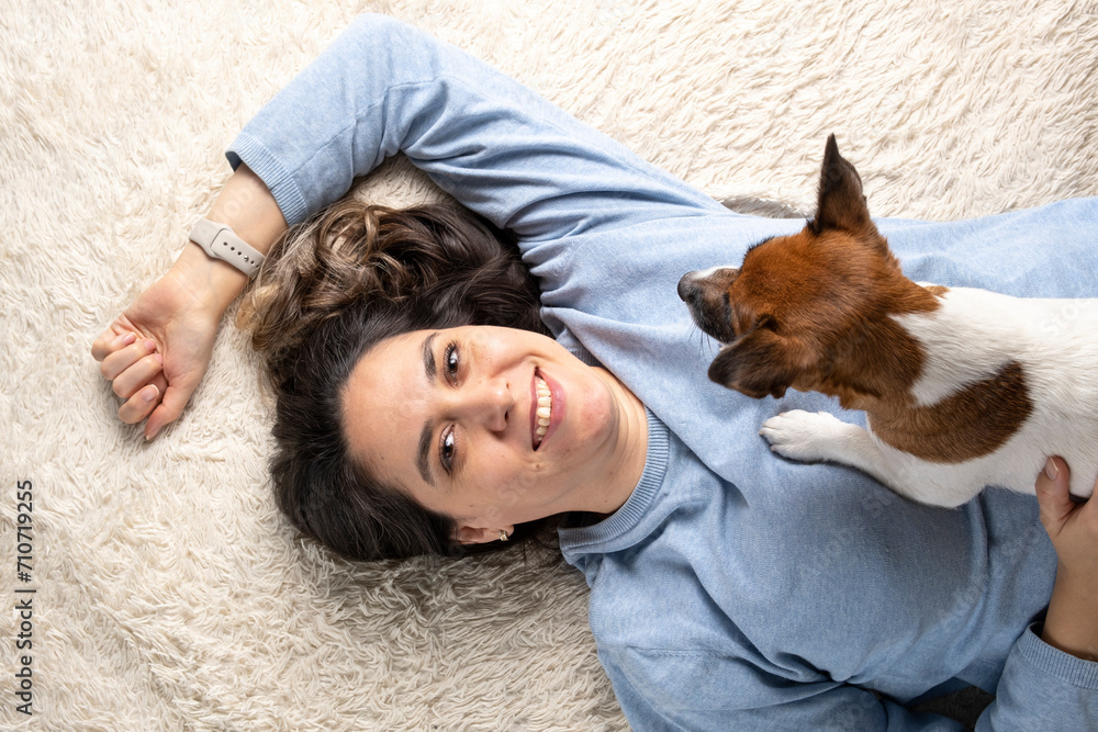 A happy young woman is lying on a bed with a small jack Russell terrier puppy. The concept of loving and caring for pets. A happy young woman is lying on a bed with a small jack Russell terrier puppy. The concept of loving and caring for pets.