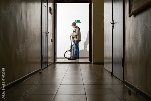 A man is vacuuming in a long hallway. The cleaner is at work. © Сергей Дудиков