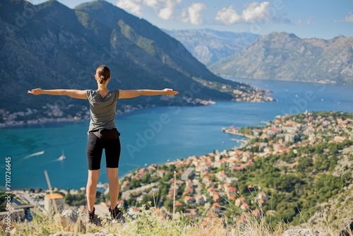 A hiker stands with open arms, embracing the breathtaking view of the Bay of Kotor and the surrounding mountains in Montenegro.