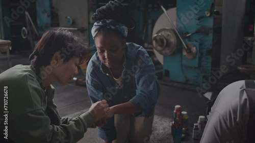 Lowkey medium shot of diverse group of female plant workers drawing feminist signs on their wrists while preparing to go on industrial strike together and fight for liberationLowkey medium shot of div photo