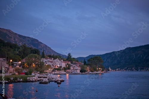 As evening falls, the tranquil seaside village of Kotor is softly illuminated, with the calm waters of the bay reflecting the last light of day.