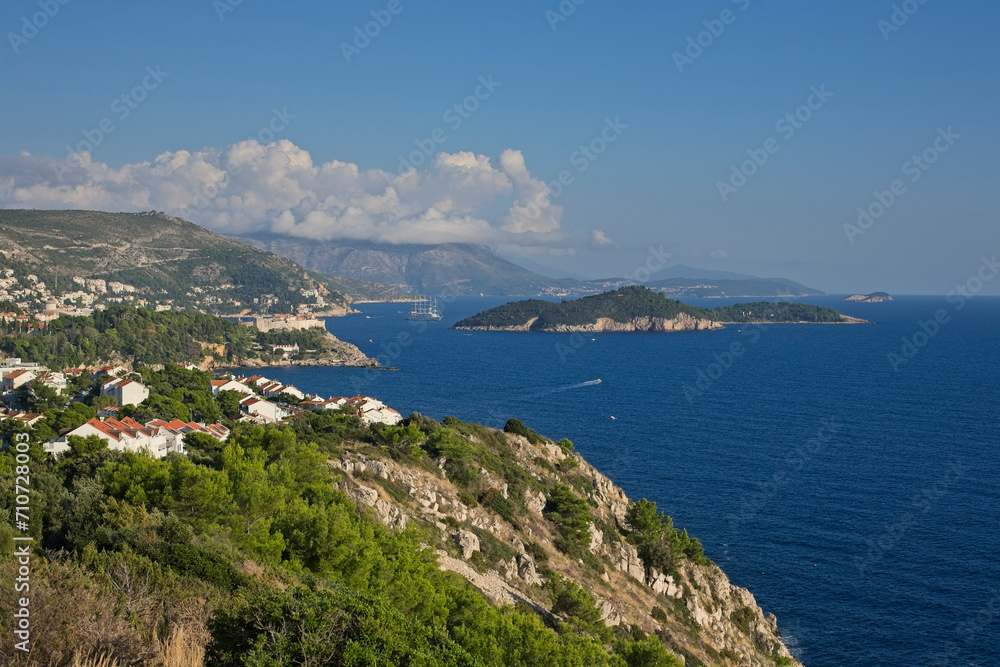 Panoramic view of Dubrovnik’s coastline, with its clear blue waters and lush green cliffs, under a sky with clouds.