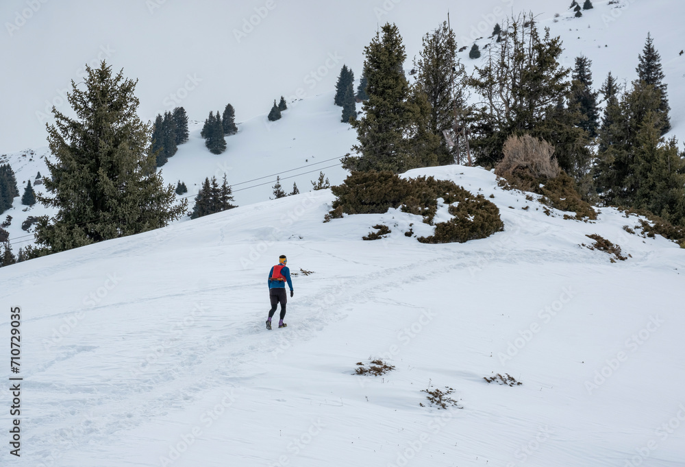 A man in sports gear climbs the snowy slope to the top of the mountain. Ziniy mountaineering is not far from Almaty. Climbing to the top of the winter mountains.