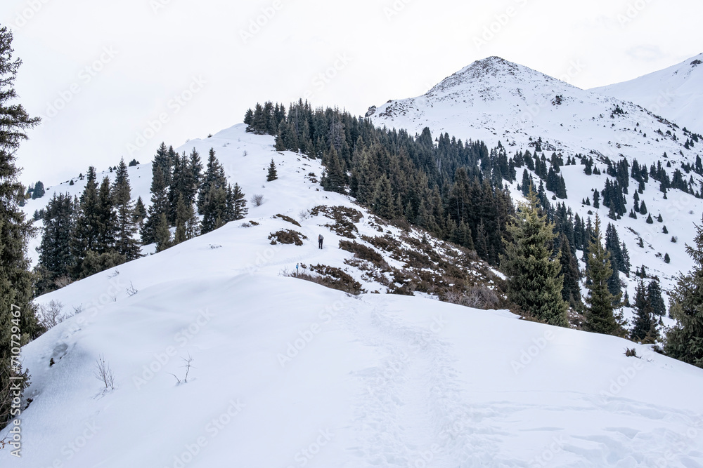 A man in sports gear climbs the snowy slope to the top of the mountain. Ziniy mountaineering is not far from Almaty. Climbing to the top of the winter mountains.