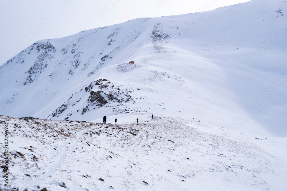 A group of people in sports equipment climb a snowy slope to the top of a mountain. Winter mountaineering is located near Almaty. Climbing to the top of the mountain in winter.