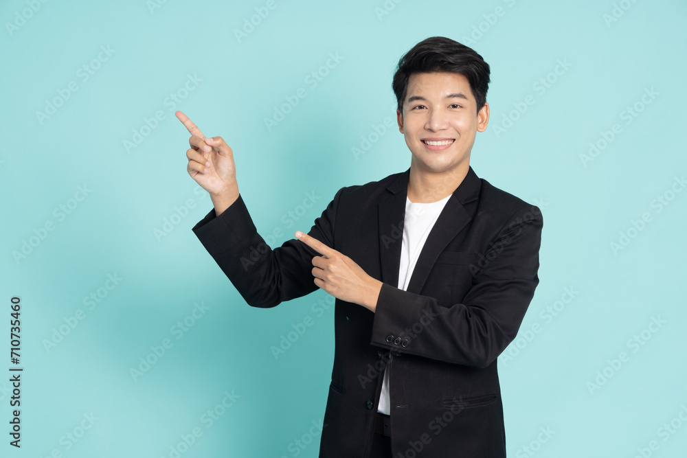 Young Asian businessman smiling and pointing to empty copy space isolated on green background Young Asian businessman smiling and pointing to empty copy space isolated on green background