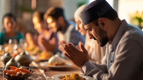 Close-up of Muslim man praying with his family at dining table.