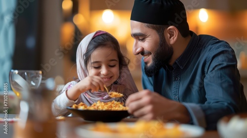 Happy Middle eastern father feeds his daughter during dinner at dining table on Ramadan.