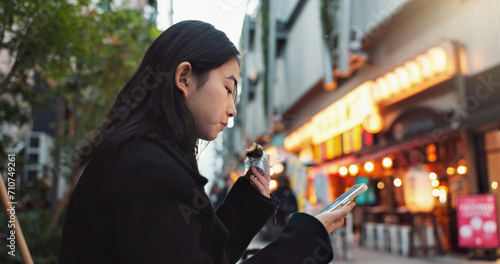 Phone, eating and Asian woman with onigiri in the city on exploring vacation, adventure or holiday. Hungry, food and young female person enjoying a Japanese snack or meal in town on weekend trip. photo