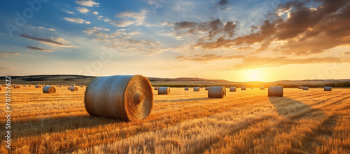 Rural farm background with hay bales at sunset. Rustic countryside view with a stunning sunset above a vast field of rolled straw