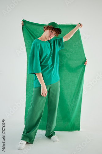 Studio creative portrait shoot of a young guy in green t-shirt and green cap green pants green clothes on green background