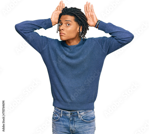 Young african american man wearing casual winter sweater doing bunny ears gesture with hands palms looking cynical and skeptical. easter rabbit concept. photo