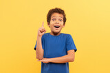 Excited boy with eureka moment, pointing up on yellow background