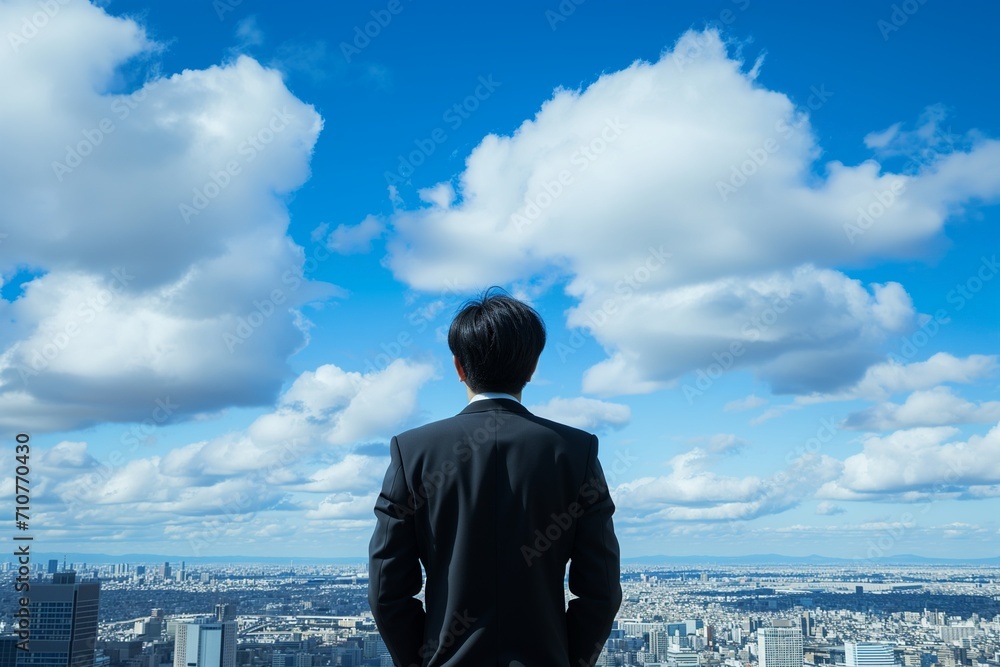 A businessman behind looking for town and blue-sky clouds on building top views. A businessman behind looking for town and blue-sky clouds on building top views.