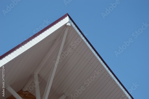 Part of the ridge of a white roof of a wooden house against a blue sky. Vacation home.Part of the ridge of a white roof of a wooden house against a blue sky. Vacation home.