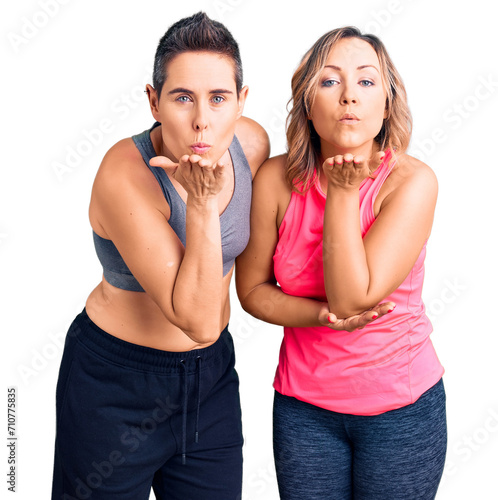 Couple of women wearing sportswear looking at the camera blowing a kiss with hand on air being lovely and sexy. love expression.