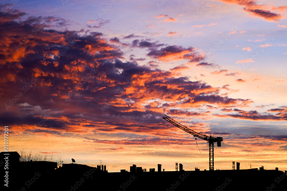 Naklejka premium Vibrant sunset over a silhouette of urban skyline with crane.