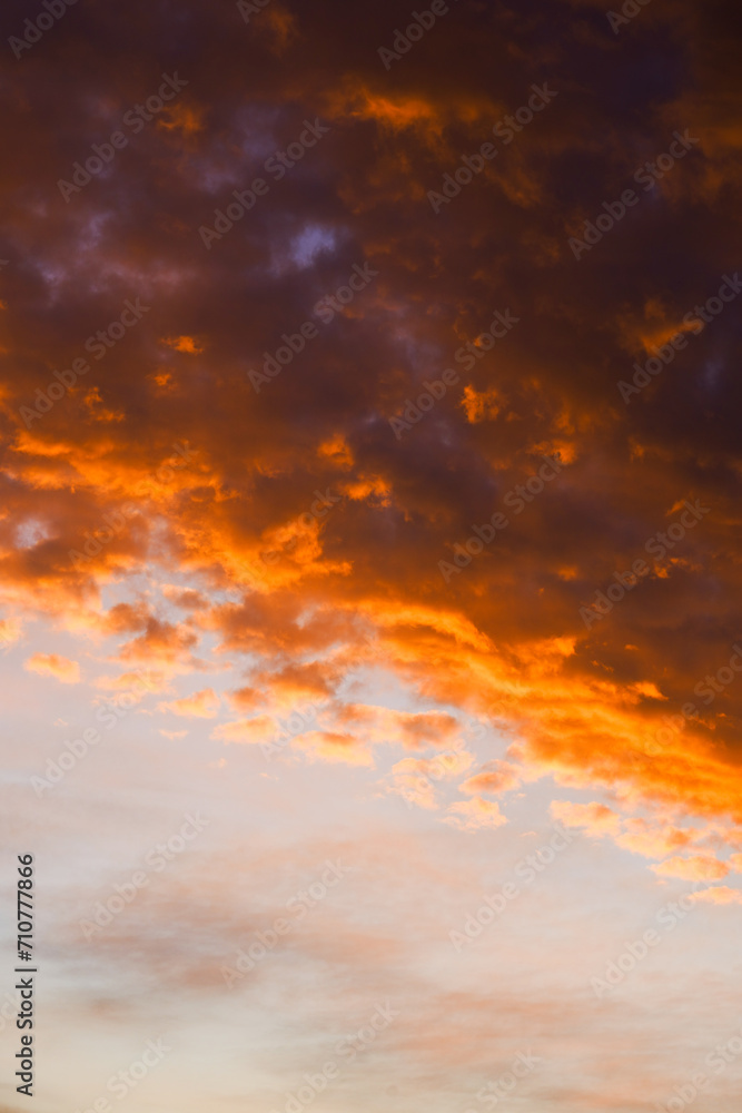 Dark clouds at sunset with fiery orange edges against a soft sky.