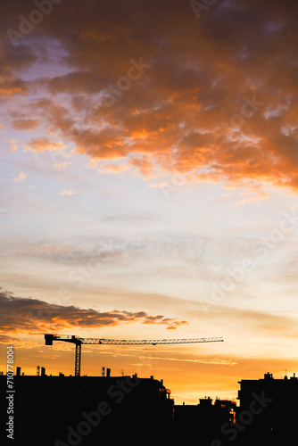 Sunset paints the sky with orange above a city silhouette and crane.