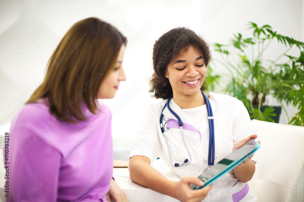Beautiful young mixed race female doctor with pregnat patient sitting in front of attendee, showing prescription on form. Beautiful young mixed race female doctor with pregnat patient sitting in front of attendee, showing prescription on form.
