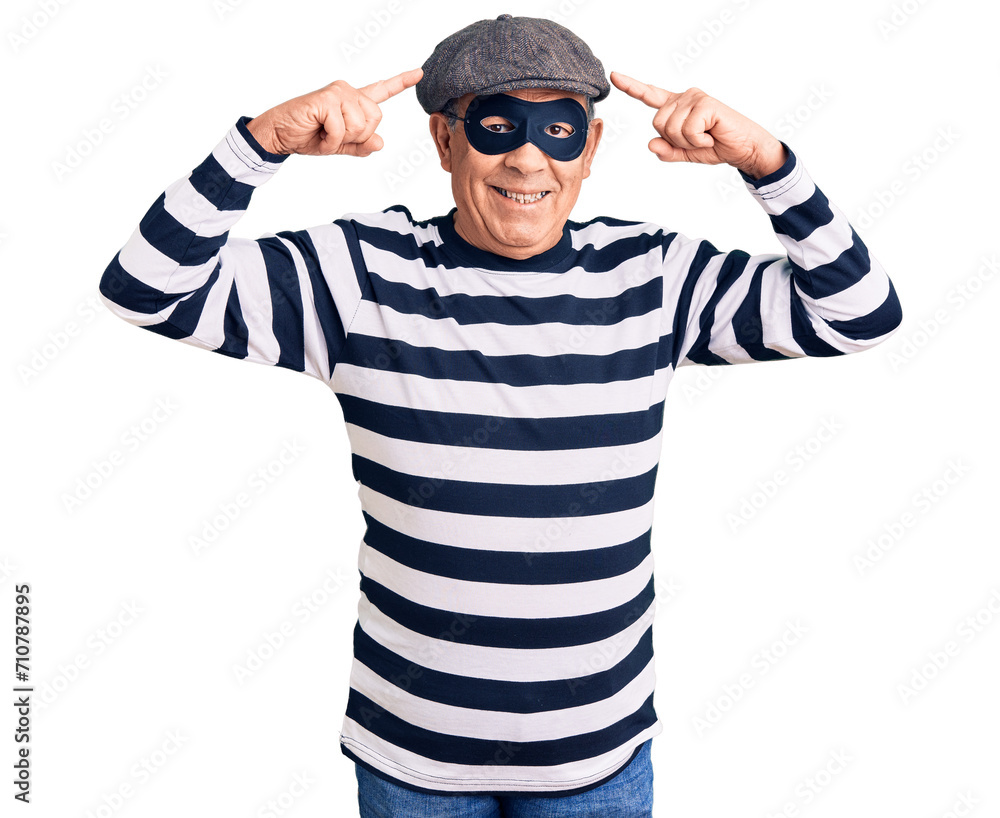 Senior handsome man wearing burglar mask and t-shirt smiling pointing to head with both hands finger, great idea or thought, good memory Senior handsome man wearing burglar mask and t-shirt smiling pointing to head with both hands finger, great idea or thought, good memory