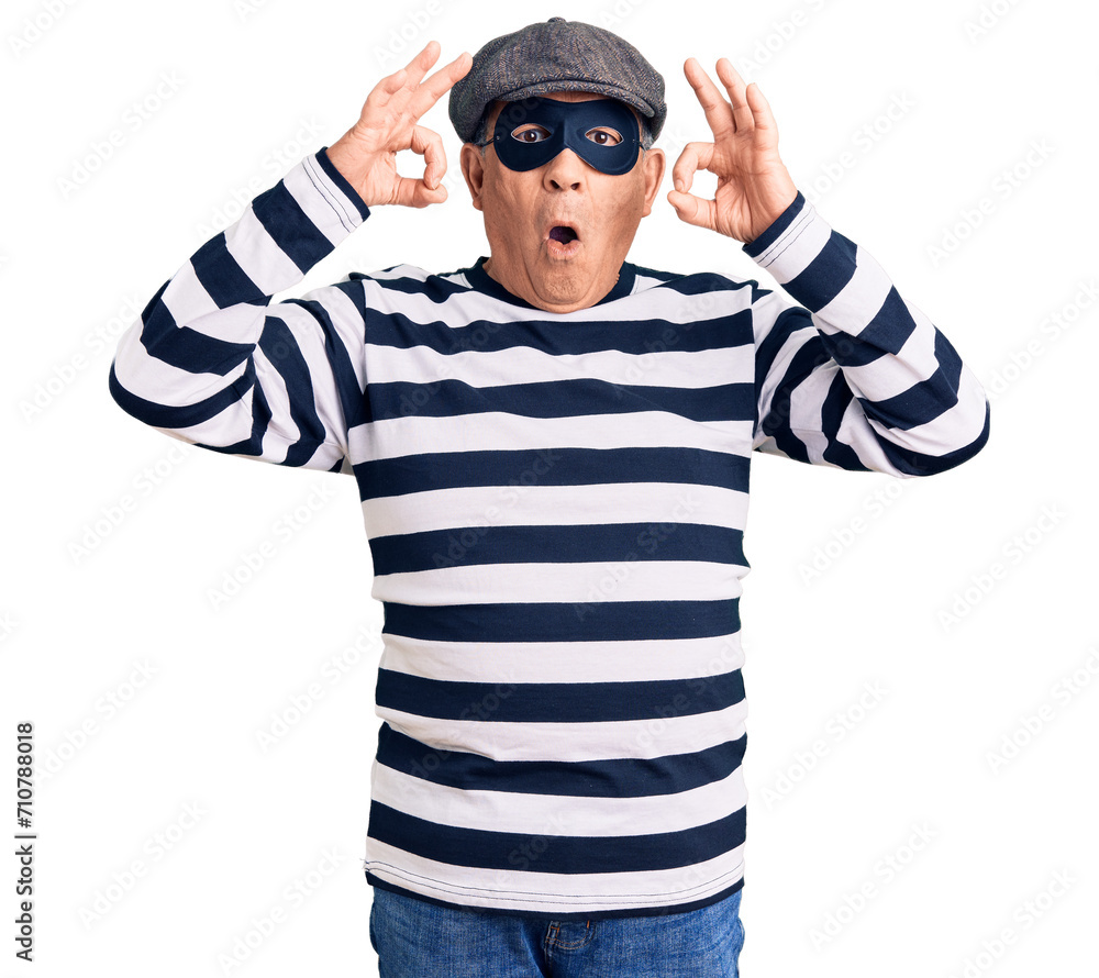 Senior handsome man wearing burglar mask and t-shirt looking surprised and shocked doing ok approval symbol with fingers. crazy expression Senior handsome man wearing burglar mask and t-shirt looking surprised and shocked doing ok approval symbol with fingers. crazy expression