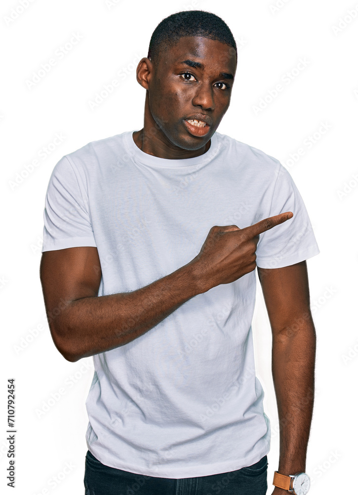 Young african american man wearing casual white t shirt pointing aside worried and nervous with forefinger, concerned and surprised expression Young african american man wearing casual white t shirt pointing aside worried and nervous with forefinger, concerned and surprised expression
