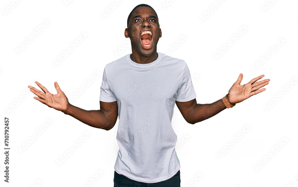 Young african american man wearing casual white t shirt crazy and mad shouting and yelling with aggressive expression and arms raised. frustration concept. Young african american man wearing casual white t shirt crazy and mad shouting and yelling with aggressive expression and arms raised. frustration concept.
