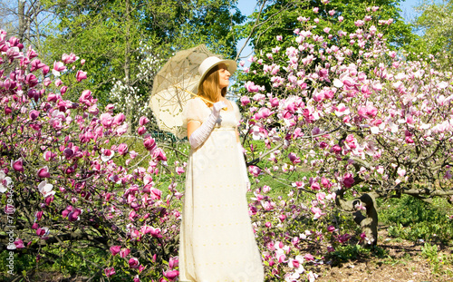 Woman in white dress in garden with pink magnolia trees in blossom.