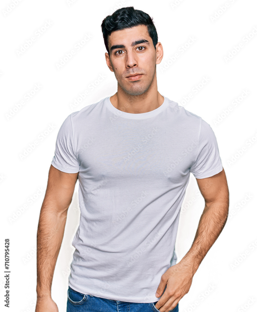 Handsome hispanic man wearing casual white t shirt relaxed with serious expression on face. simple and natural looking at the camera. Handsome hispanic man wearing casual white t shirt relaxed with serious expression on face. simple and natural looking at the camera.