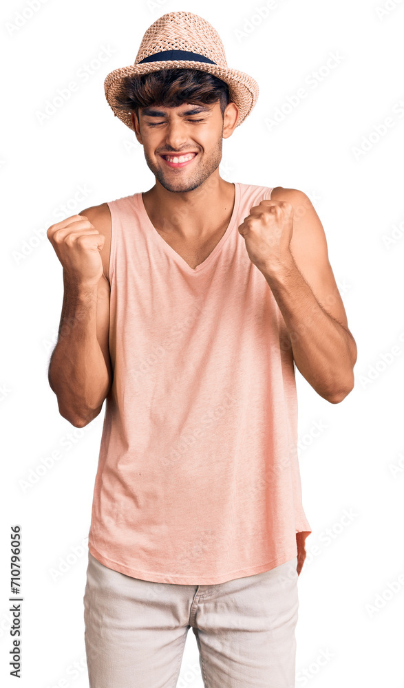 Young hispanic man wearing summer hat very happy and excited doing winner gesture with arms raised, smiling and screaming for success. celebration concept. Young hispanic man wearing summer hat very happy and excited doing winner gesture with arms raised, smiling and screaming for success. celebration concept.