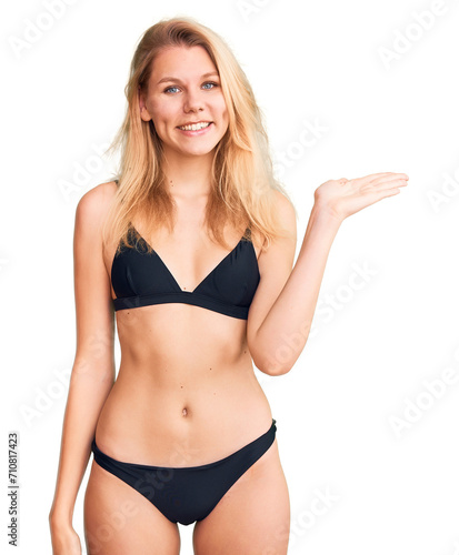 Young beautiful blonde woman wearing bikini smiling cheerful presenting and pointing with palm of hand looking at the camera. © Krakenimages.com
