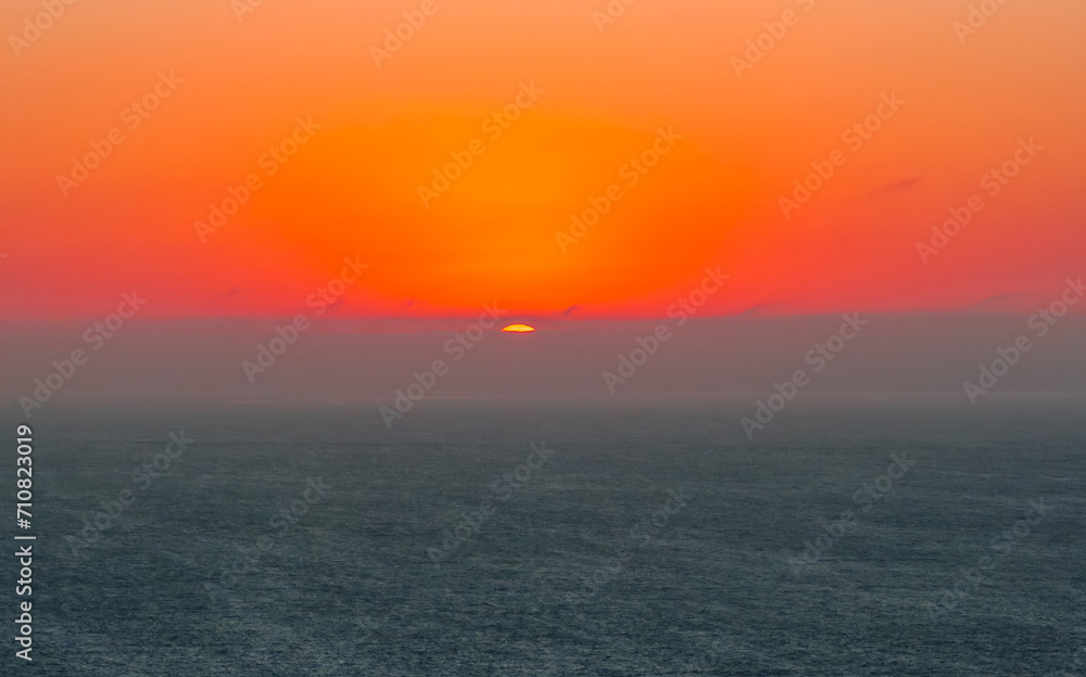 Bright sunset with large yellow sun under the Pacific ocean. Orange and golden sunset sky calmness tranquil relaxing sunlight summer mood.