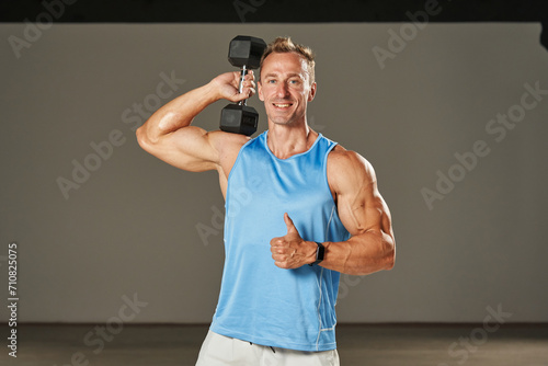 A young man, sculpted and strong, wields dumbbells with focus and determination, exemplifying his dedication to a rigorous fitness regimen that keeps him in peak physical condition.